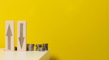 two wooden bars with arrows up and down on the table with coins, yellow background. Falls and increases in prices for utilities photo
