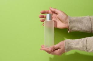 female hand holds empty plastic container for liquid products, soap or shampoo on a green background photo