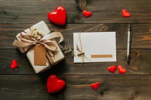 caja de regalo y tarjeta de felicitación con cinta de lazo y corazones de papel en la mesa de madera para el día de san valentín. copie el espacio foto