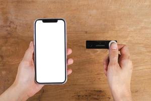 Hand holding mobile phone and hardware wallet on wooden table photo