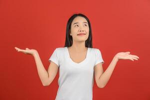 Portrait of young asian woman pointing with two hands and fingers to the side over isolated red background photo