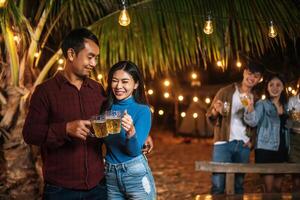 Portrait of Happy Asian friends having dinner party together - Young people toasting beer glasses dinner outdoor  - People, food, drink lifestyle, new year celebration concept. photo