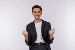 Portrait of happy joyful young businessman standing doing winner gesture clenching fists keeping isolated on white color wall background studio photo