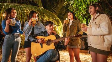 Portrait of Happy Asian group of friends having fun to music dining and drinking together outdoor - Happy friends group toasting beers  - People, food, drink lifestyle, new year celebration concept. photo