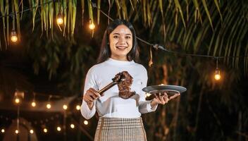 Portrait of Happy Asian young woman cooking meat on barbecue grill at new year party. Bar-B-Q or BBQ on traditional stove. Night Party, people and celebration concept. photo