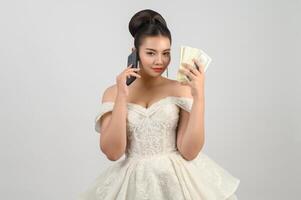 Young asian beautiful bride posting with smartphone and banknote in hand photo