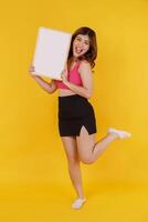 Portrait of Happy young woman holding an empty white placard over isolated yellow background. photo