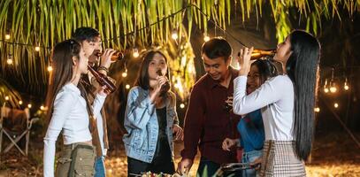 felices amigos asiáticos animando con una cena de barbacoa al aire libre - grupo de personas divirtiéndose en la fiesta de año nuevo. gente, comida y bebida concepto de estilo de vida fiesta nocturna, gente y concepto de celebración. foto