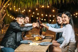 retrato de felices amigos asiáticos cenando juntos - jóvenes sentados en la mesa del bar brindando vasos de cerveza cenando al aire libre - gente, comida, estilo de vida de bebida, concepto de celebración de año nuevo. foto