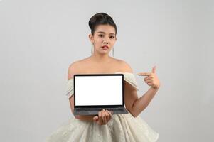 Young asian beautiful bride pose with mockup laptop computer in hand photo