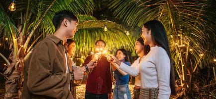 Portrait of Happy Asian group of friends having fun with sparklers outdoor - Young people having fun with fireworks at night time  - People, food, drink lifestyle, new year celebration concept. photo