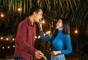 Happy Asian couple cheering with barbecue dinner outdoor - Group of people having fun in new year party. People, food and drink lifestyle concept Night Party, people and celebration concept. photo