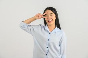 retrato de una joven asiática feliz con camisa azul haciendo símbolo de paz con los dedos sobre la cara aislada de fondo blanco foto