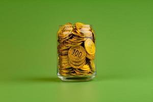 Saving gold coins in glass jars on green background, coin savings concept photo