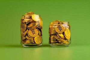 Saving gold coins in glass jars on green background, coin savings concept photo