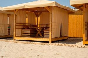 Wooden tents on the sandy beach. Cafe. Restaurant. Shady place for food on the coast. Shelter from the sun. photo