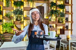 camarera con protector facial, la visera sirve el café en el restaurante durante la pandemia del coronavirus que representa un nuevo concepto normal foto