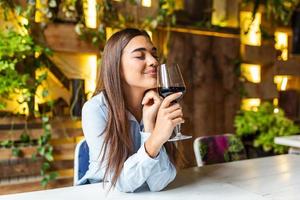 hermosa mujer degustando vino mientras está sentado en el restaurante. imagen de una linda mujer joven sentada en un café sosteniendo un vaso y bebiendo vino. retrato de una hermosa mujer turista de cata de vinos. foto