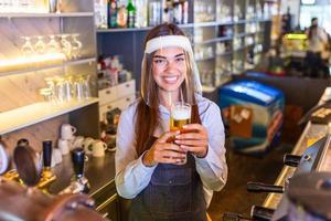 camarero con protección facial covid-19, sirviendo una cerveza de barril en el mostrador del bar durante la pandemia del coronavirus, estantes llenos de botellas con alcohol en el fondo foto