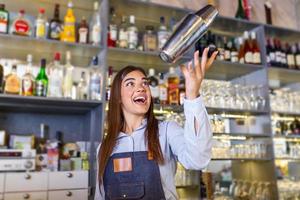 Beautiful female bartender tosses cocktails shaker into the air and arranges a real show for their guests photo