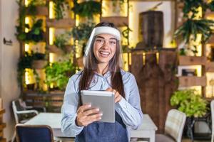 Happy female waitress using digital tablet while wearing visor at the restaurant or cafe. Open again after lock down due to outbreak of coronavirus covid-19, New normal photo