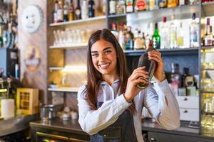 joven trabajadora en el mostrador de la camarera en el bar del restaurante preparando un cóctel con agitador. bella joven detrás de la barra haciendo un cóctel foto