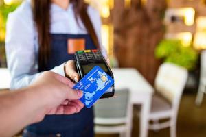 Contactless payment concept, female holding credit card near nfc technology on counter, client make transaction pay bill on terminal rfid cashier machine in restaurant store, close up view photo