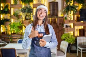 Happy female waitress using digital tablet while wearing visor at the restaurant or cafe. Open again after lock down due to outbreak of coronavirus covid-19, New normal photo