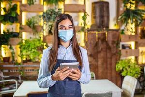 Happy female waitress using digital tablet while wearing protective face mask at the restaurant or cafe. Open again after lock down due to outbreak of coronavirus covid-19, New normal photo