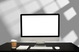 Computer monitor with white blank screen putting on white working desk with wireless mouse and keyboard over blurred modern office as background. photo