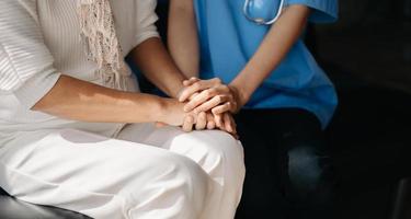 Medical doctor holing senior patient's hands and comforting her at home photo