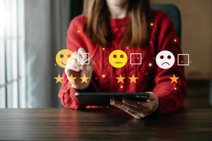 una mujer inteligente usa un smartphone y una tableta eligiendo un icono de cara de sonrisa feliz. calificación de comentarios y experiencia positiva de revisión del cliente, evaluación de salud mental. foto