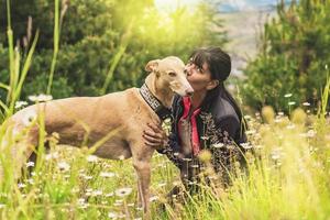 Latin woman kissing her dog outdoors. Sunset sunlight in nature. photo