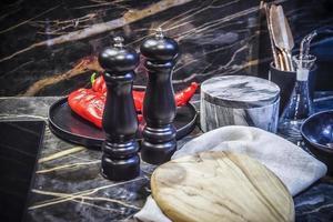 A modern dark kitchen top with various kitchen utensils, boards, salt and pepper shaker and red peppers photo