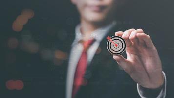 Wooden block in businessman hand and arrow icon hitting center of dartboard target,Setting business goals and focused concepts, Organizational growth and objectives, marketing strategy planning photo