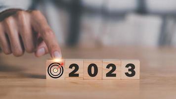Businessman hand pointing at wooden block and arrow icon hitting center of dartboard target, Setting business goals and focused concepts, Organizational growth and goals in 2023 photo