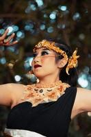 A beautiful Javanese woman poses with her hand in a black costume while wearing a golden crown and golden necklace photo