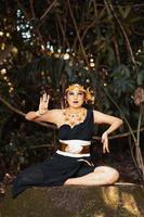 Indonesian woman sitting on the rock in a black dance costume while wearing a golden crown and golden necklace photo