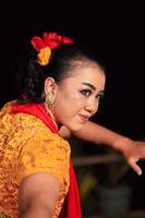 hermoso rostro de una mujer indonesia maquillada mientras baila una danza tradicional con un traje naranja durante el festival foto