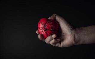 concepto doloroso, tristeza, falta de libertad. mucha angustia y tristeza. mano sosteniendo y apretando un corazón rojo con alambre de cobre desordenado atado. tono oscuro foto