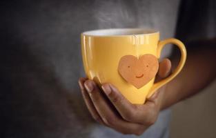 Tea Lover Concept. Hand Holding a Cup of Tea. Eco-Friendly Style Tag made as Heart Shape and Hanging on Cup. Green, Oolong, Fermented, Organic, Healthy and Aromatic Tea photo