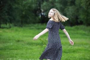 niña feliz en un vestido romántico en un prado verde de verano. hermosa jovencita sonríe y mira a la cámara. foto