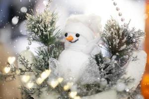 divertido muñeco de nieve en el fondo de ramas de árboles de navidad y bokeh. foto