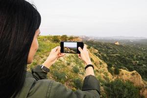 Female persons hands are holding the smartphone and taking photo of beautiful nature landscape on tour around VAshlovani national park. Smartphone photography and using grid mode