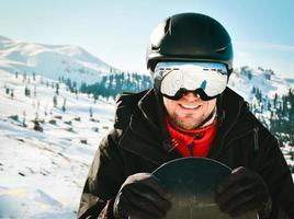 Close up portrait caucasian man with the reflection of snowed mountains, white slope and ski resort. A mountain range reflected in the ski mask. Portrait of man at the ski resort photo