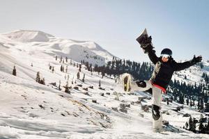 Snowboarder holding his snowboard over head kick snow happy feeling great in ski resort excited on holiday vacation solo. Sunny weather powder day photo