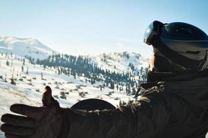 Male person alone in winter skiing outfit exited enjoys panorama of mountains with spreaded hands. Snowboard in forest and caucasus mountains photo