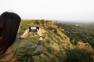 Caucasian woman hold smartphone take photo of beautiful nature outdoors on holiday vacation. Use different photo modes on screen tap record capture button