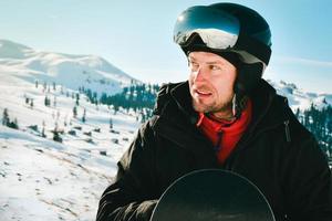 Close up portrait caucasian man with the reflection of snowed mountains, white slope and ski resort. A mountain range reflected in the ski mask. Portrait of man at the ski resort photo