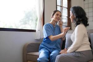 Asian nurse showing health checkup report to grandmather and giving advice. medical assisted living visit senior patient at home. Home nursing and healthcare caregiver concept photo